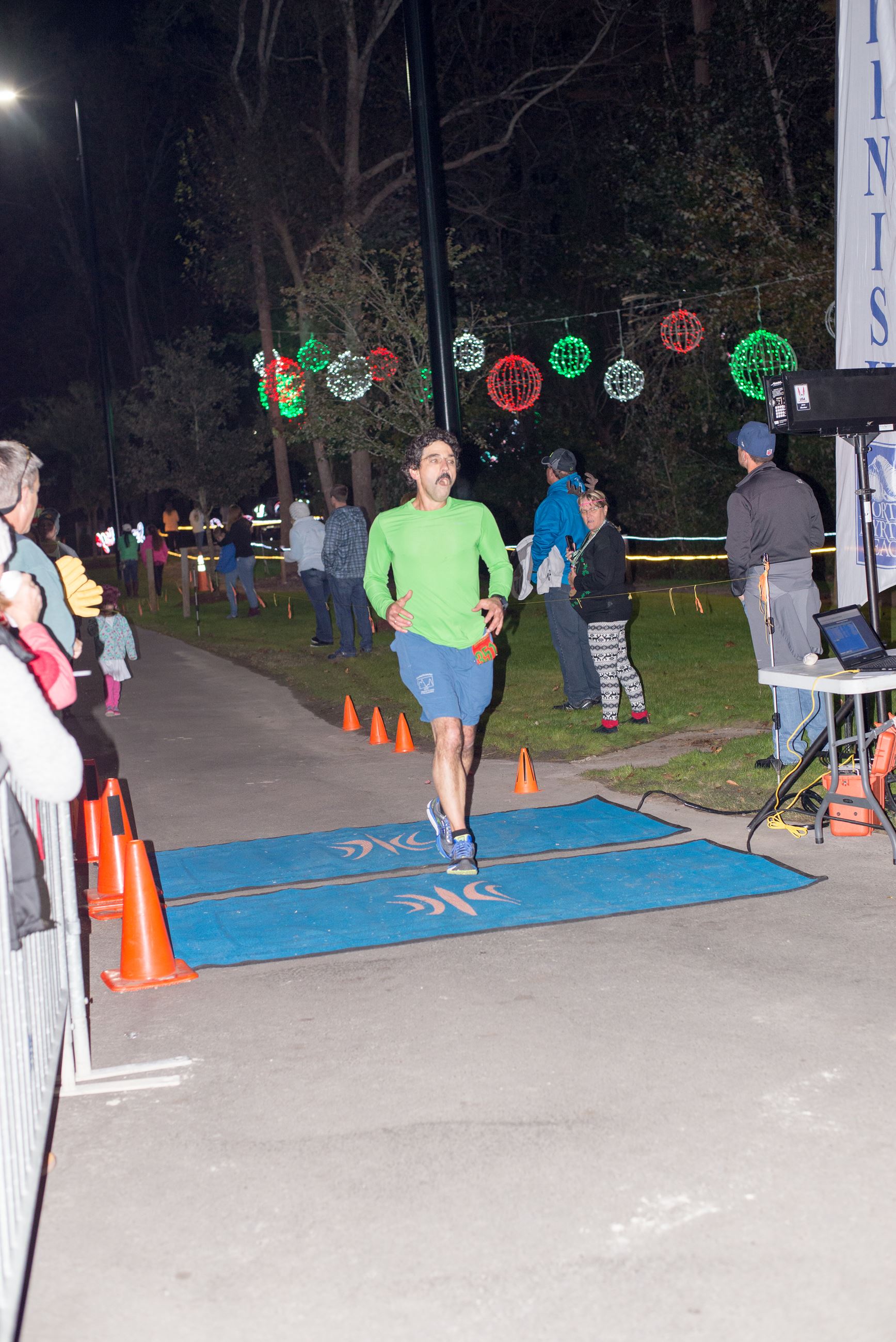 Man in Blue Shorts and Green Shirt Running Across a Finish Line